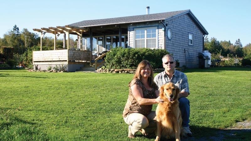 Debbie and Mike Cameron pose with their five-year-old golden retriever, Ben, in front of their off-grid home near Pugwash, Nova Scotia.