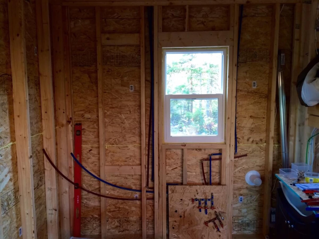 Red and blue PEX pipes in the unfinished bathroom wall beneath a window