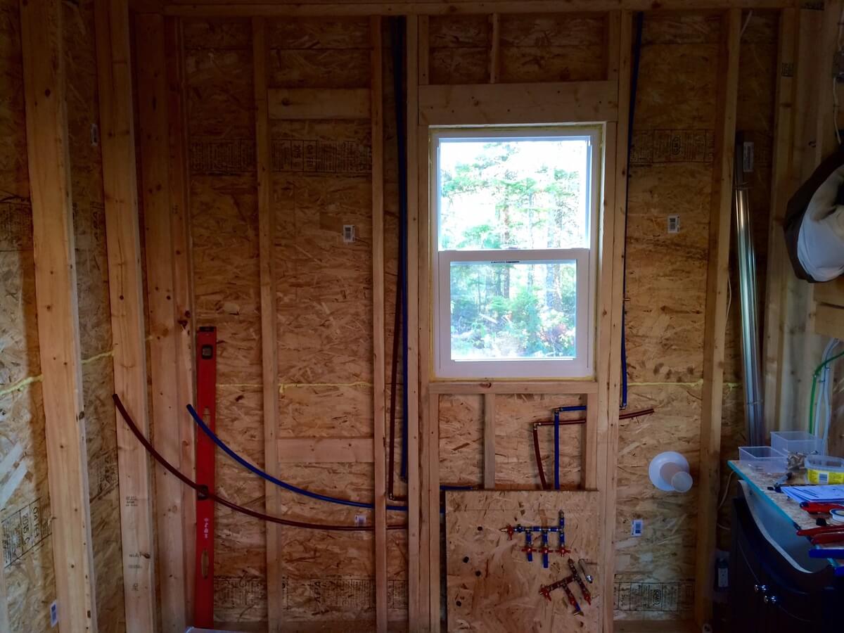 Red and blue PEX pipes in the unfinished bathroom wall beneath a window
