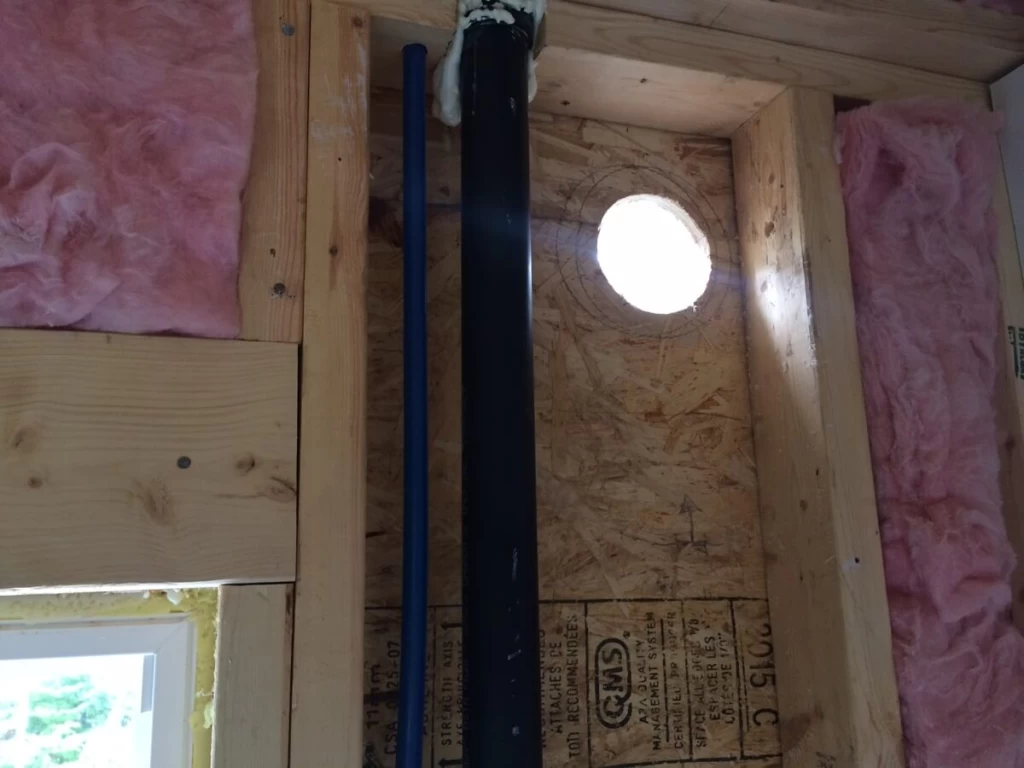 Circular wall opening beside plumbing and framing during the 2016 bathroom build