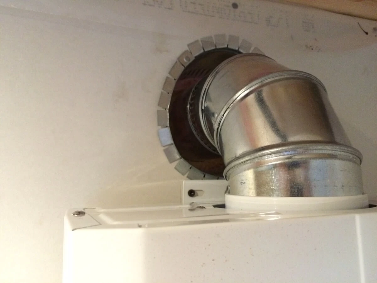 Metal exhaust elbow entering the bathroom wall above the water heater