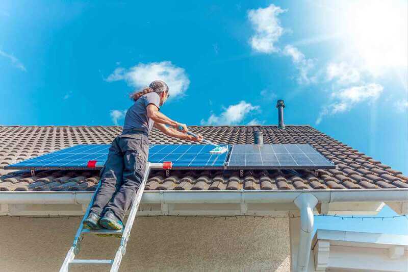 Image of man cleaning solar panels on ladder with an extension pole