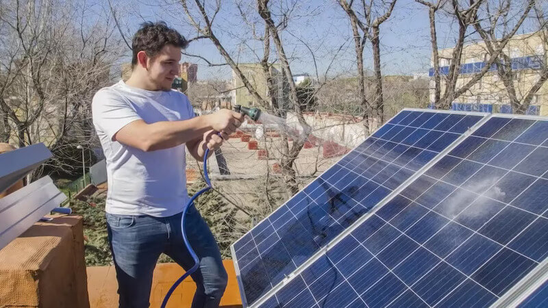 Image of man spraying water on solar panels to clean them off