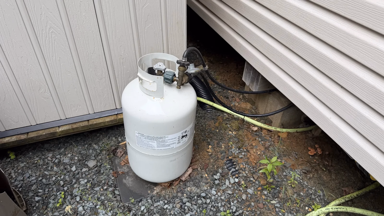 White propane cylinder with regulator and hose outside the cabin beside a storage shed