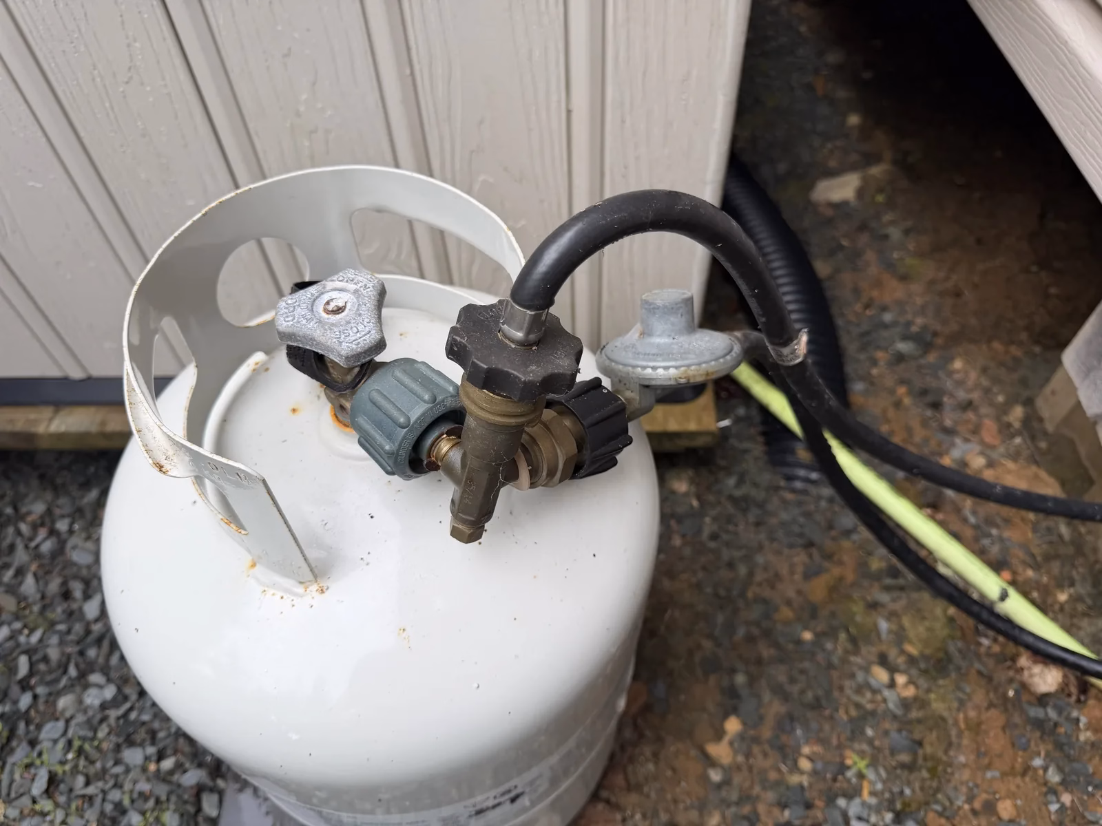 Close-up of propane cylinder valve, brass fittings, grey regulator and black hose